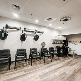A modern salon interior with a row of chairs and wall-mounted hair dryers.