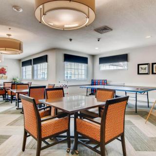 A spacious game room featuring a ping pong table, tables with orange chairs, and stylish lighting.