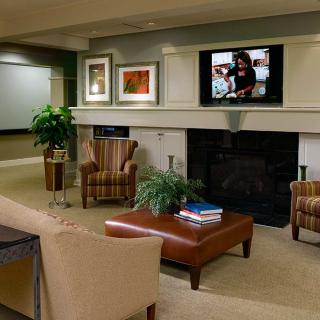 A cozy living room with a sofa, armchairs, and a coffee table facing a fireplace topped with a television.