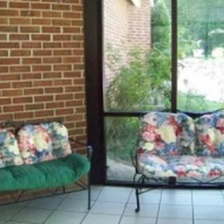 A cozy patio area with floral and green cushioned seating against a brick wall and large glass windows.
