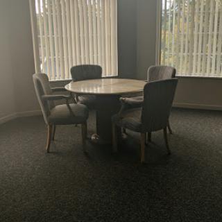 A cozy meeting room with a round table and four chairs, illuminated by natural light from the blinds.