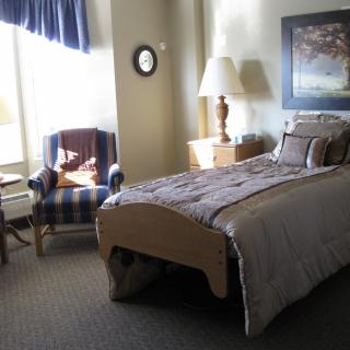 A cozy bedroom with a single bed, bedside table lamp, and a chair by the window.