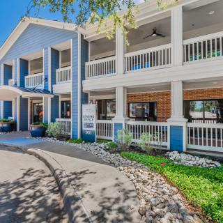 A two-story building with blue and white exterior featuring balconies and landscaped surroundings.