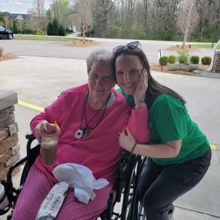 An elderly woman in a wheelchair enjoying time with a younger woman outdoors.