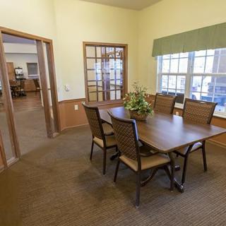 A cozy dining area with a wooden table and chairs, featuring large windows and a decorative plant centerpiece.