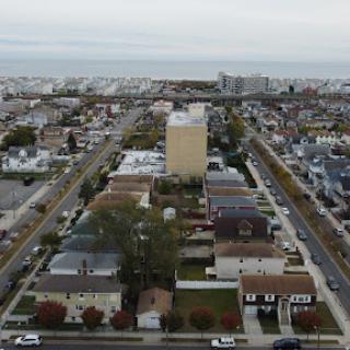 An aerial view of a suburban cityscape showcasing residential buildings and roads, with a hint of the coast in the distance.
