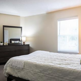 A cozy bedroom with a bed, dresser, and a mirror near a window.
