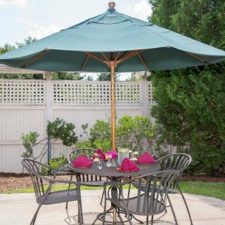 A patio set with a table and chairs under a large umbrella in a garden setting.