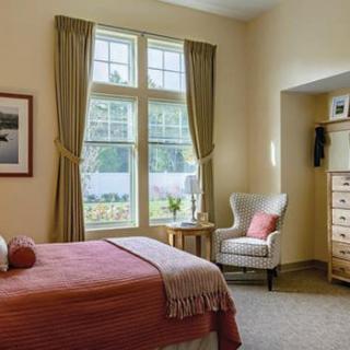 A cozy bedroom with a bed, armchair, and large window overlooking a garden.