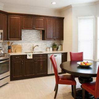 A modern kitchen featuring dark cabinetry, a round dining table with red chairs, and a stylish backsplash.