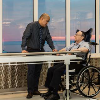 A caregiver engages with a patient in a wheelchair as the sun sets outside, highlighting a moment of support and connection.