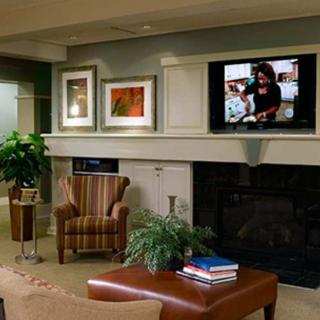 A cozy living room with a television above the fireplace, featuring artwork and a comfortable armchair.