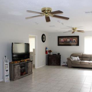 A spacious and modern living room featuring a comfortable couch, a TV setup, and ceiling fans.
