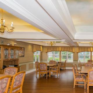 A spacious dining room with wooden tables and chairs, featuring large windows and chandeliers.