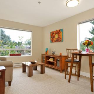 A cozy living room filled with natural light, featuring modern wooden furniture and vibrant artwork on the wall.