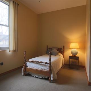 A cozy bedroom with a single bed and a warm-lit lamp by the window.