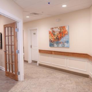 A well-lit hallway with a wooden door, adorned with a colorful painting on the wall.
