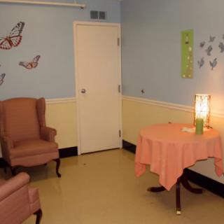 A cozy room with pastel walls, featuring comfortable chairs, a small table with a lamp, and butterfly decorations.