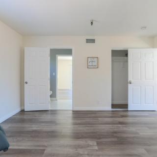 An empty room with hardwood flooring, featuring two open doors leading to a closet and hallway.
