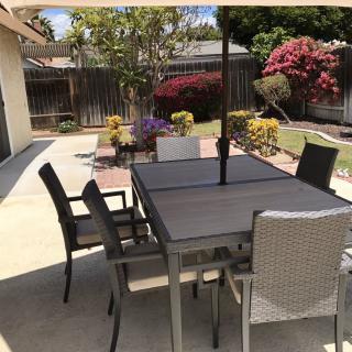 A backyard patio with a table, chairs, and an umbrella, surrounded by a garden.