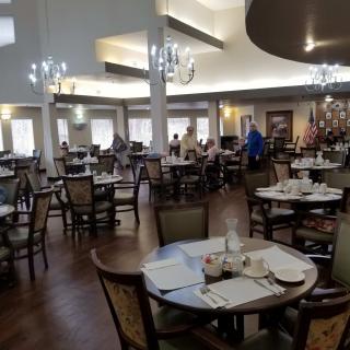 A spacious dining area with neatly arranged tables and chairs, softly lit by chandeliers.