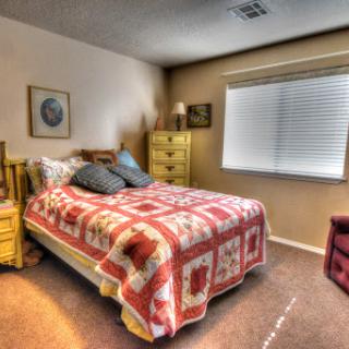 A cozy bedroom featuring a bed with a colorful quilt, a dresser, and natural light coming through the window.