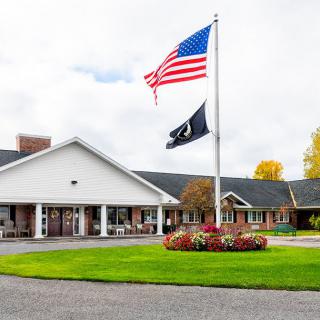 A building with American and POW flags flying in the forefront, surrounded by a well-maintained lawn.