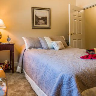A cozy bedroom with a neatly made bed, bedside table, and warm lighting.