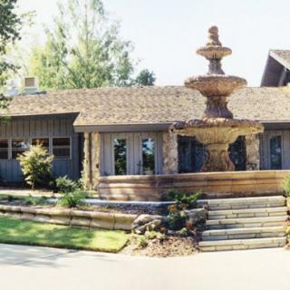 A charming house with a prominent fountain in the front yard, surrounded by lush landscaping and trees.
