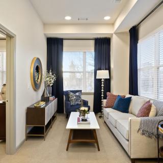 A modern living room with neutral tones, featuring a comfortable sofa, stylish coffee table, and floor lamp. The space is enhanced by blue curtains and ample natural light.