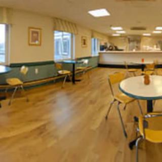 A spacious cafeteria with wooden flooring, tables, and chairs.