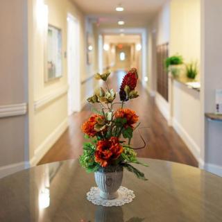 A flower arrangement in a vase sits on a table in a well-lit hallway.