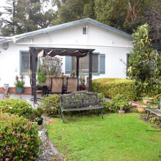 A charming white house surrounded by a well-maintained garden with seating areas.