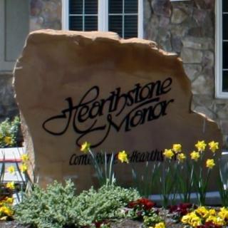 A decorative stone sign with 'Hearthstone Manor' inscribed, surrounded by blooming flowers.