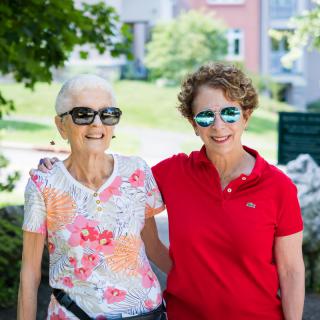 Two women smiling and wearing sunglasses while enjoying a sunny day outdoors.