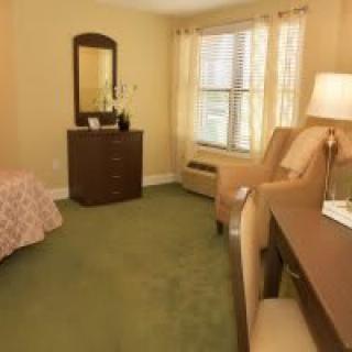 Cozy bedroom interior with a bed, dresser, chairs, and natural light from the window.