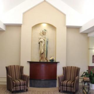 A serene interior space featuring a statue in a wall niche flanked by two chairs.