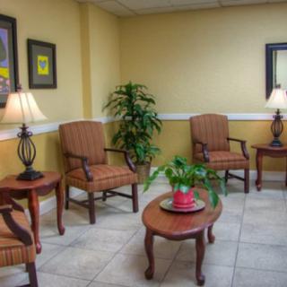 A cozy waiting room with comfortable chairs, a central table, lamps, and decorative plants.