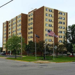 A multi-story residential building surrounded by trees and flags.