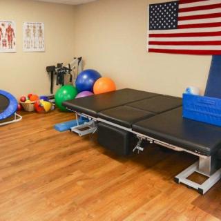 A physical therapy room equipped with exercise balls, a trampoline, and a therapy bed, decorated with an American flag on the wall.
