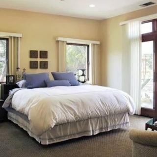 A cozy bedroom with a large bed, featuring soft pillows and a comforter, illuminated by natural light through multiple windows.