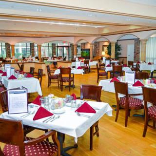 An elegantly set restaurant dining room with tables covered in white tablecloths and arranged neatly.