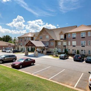 A residential building with a parking lot and several cars under a blue sky with scattered clouds.