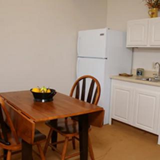 A kitchen space with a wooden dining table, chairs, a refrigerator, and cabinets.