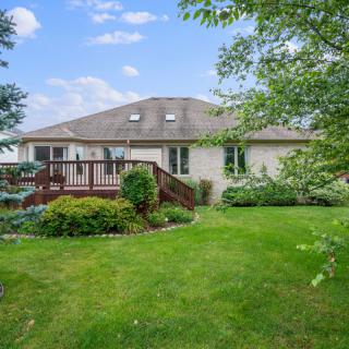 A residential house with a spacious backyard featuring a green lawn and a wooden deck.