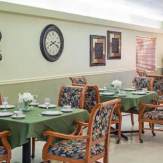 A neatly arranged dining area with tables set for a meal, featuring floral upholstered chairs and wall decor.