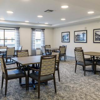 A spacious dining room with several tables and chairs, featuring artwork on the walls and ample lighting.
