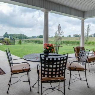 A cozy covered patio with outdoor furniture overlooking a lush green garden.