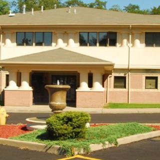 Front view of a building with a fountain and garden in the entrance area on a sunny day.
