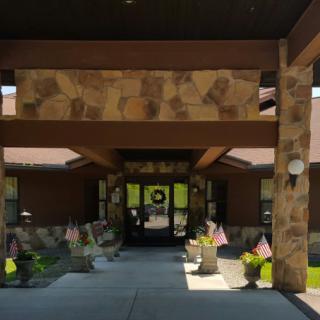 A building entrance with a stone facade, featuring a covered walkway adorned with plants and flags.